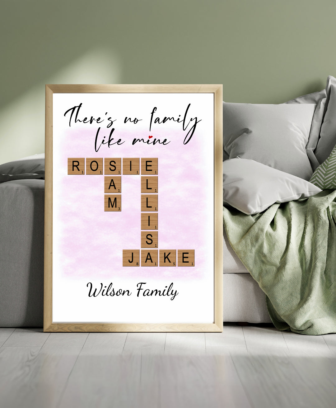 Framed family name print with Scrabble tile letters on a light background, leaning against a wall.